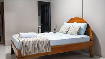 Una cama individual con cabecera de madera, ropa de cama blanca y una manta a rayas.