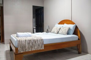 Una cama individual con cabecera de madera, ropa de cama blanca y una manta a rayas.