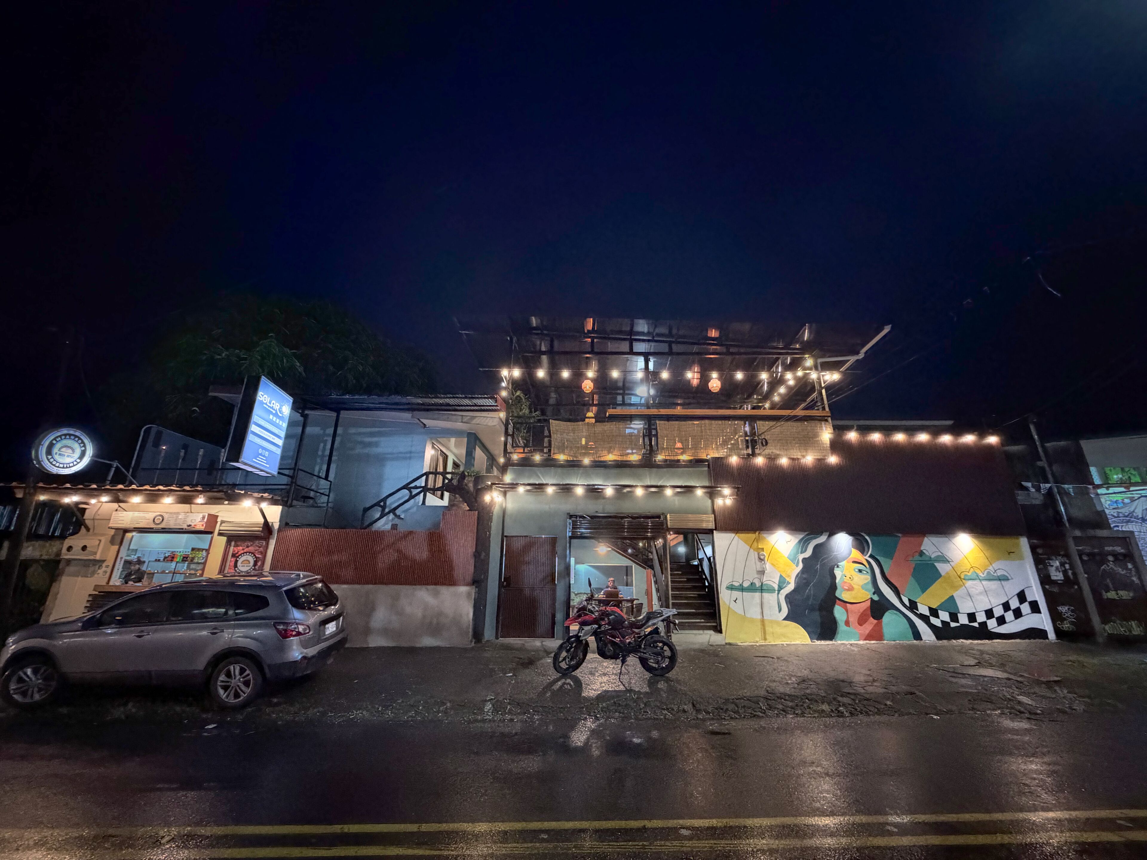 Um edifício com uma escadaria, uma moto estacionada em frente e um mural na parede.