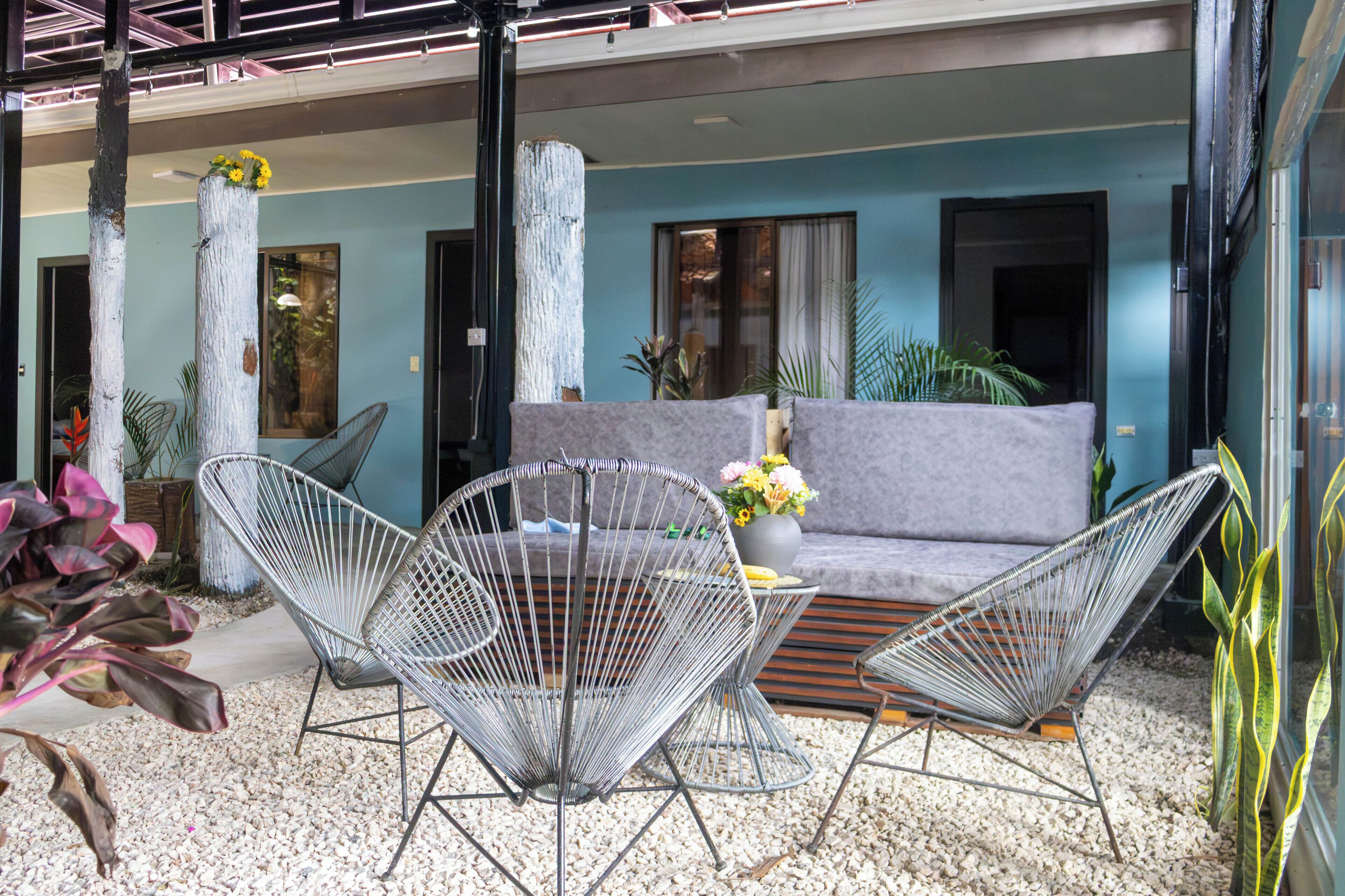 Un área de estar moderna al aire libre con sofá y sillas de estructura metálica, rodeada de plantas y un suelo de grava.