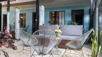 Un área de estar moderna al aire libre con sofá y sillas de estructura metálica, rodeada de plantas y un suelo de grava.