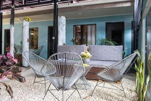 Un área de estar moderna al aire libre con sofá y sillas de estructura metálica, rodeada de plantas y un suelo de grava.