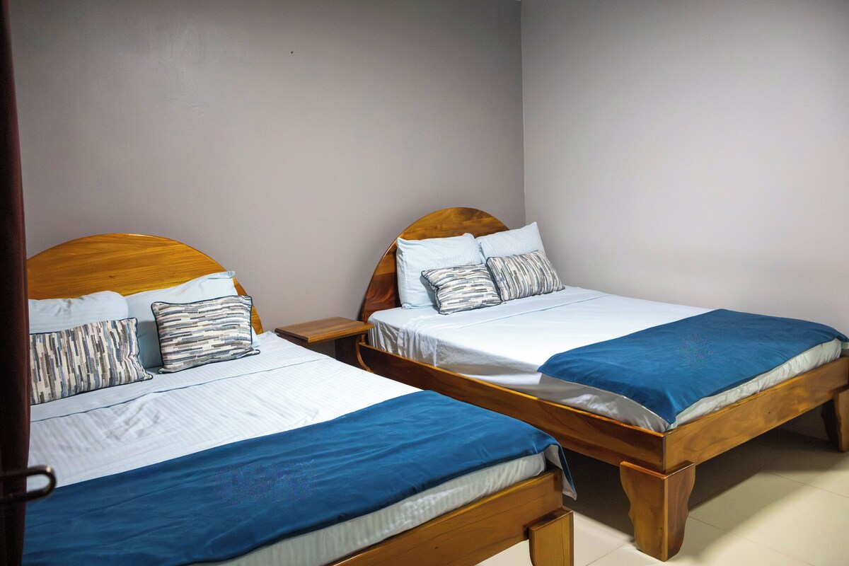 Dos camas de madera con cabeceras, ropa blanca de cama y mantas azules.