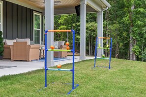 Zwei Spielgeräte im Freien mit orangefarbenen und grünen Elementen, vor einer Hausfassade und einem Rasen.