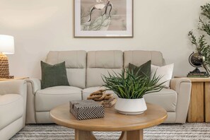 Una sala de estar con un sofá, una mesa redonda de centro, una planta en maceta y un cuadro en la pared.