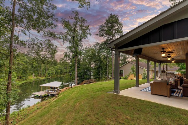 A covered outdoor patio with a view of a lake and a house in the background.