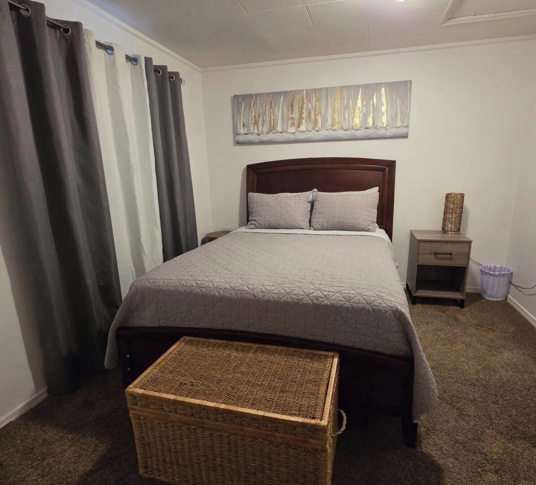 Un dormitorio con cama, mesita de noche, cubo de basura y cesta de mimbre.
