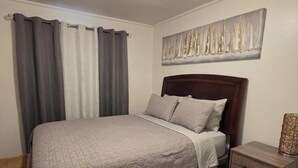 Ein Schlafzimmer mit einem Bett, Vorhängen, einem Nachttisch, einer Lampe und einem Bild an der Wand.