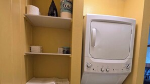 Ein Waschraum mit einer weißen Waschmaschine und einem Trockner, Regalen mit gefalteten Handtüchern und einer Flasche Kirkland Premium Handtuch.