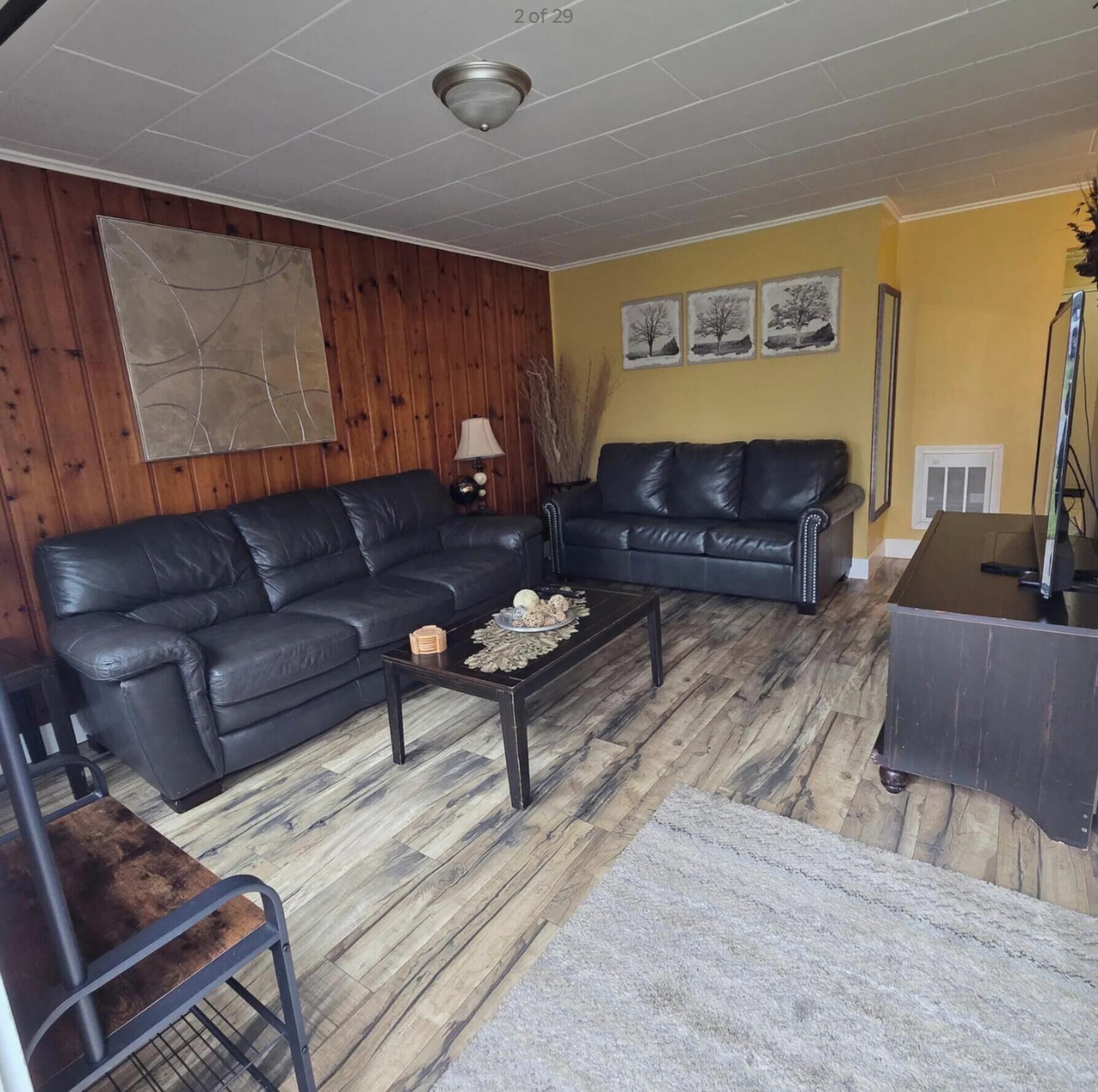 A living room with two black leather sofas, a coffee table, and a wooden floor.