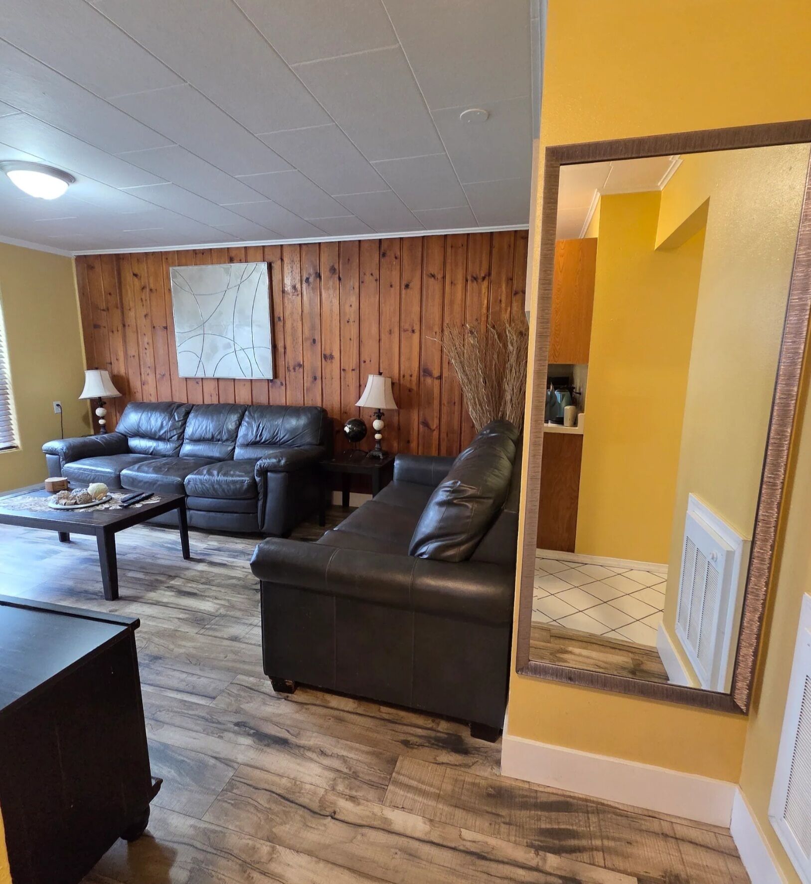 Una sala de estar con pared de paneles de madera, un sofá de cuero negro, una mesita de centro y dos lámparas.