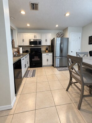 A modern kitchen with white cabinets, stainless steel appliances, and a dining area with a wooden table and chairs. - Quiet &Convenient, Close to Tampa’s Top Destinations  (Seffner)