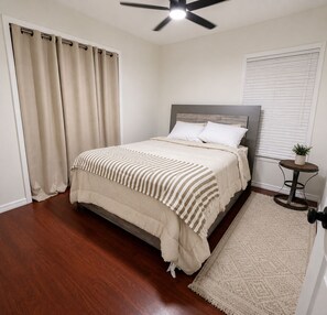 A bedroom with a bed, curtains, a ceiling fan, a bedside table with a plant, and a rug. - Quiet &Convenient, Close to Tampa’s Top Destinations  (Seffner)