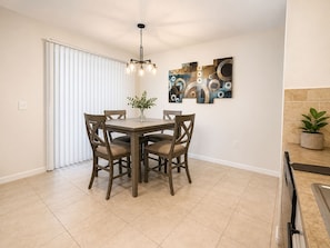 A dining area with a round table, four chairs, a chandelier, and abstract wall art. - Quiet &Convenient, Close to Tampa’s Top Destinations  (Seffner)