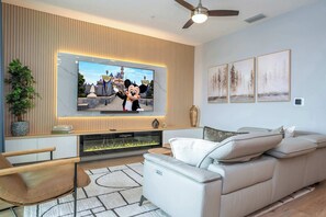 Una sala de estar moderna con una televisión de pantalla plana, chimenea, ventilador de techo y sofá.