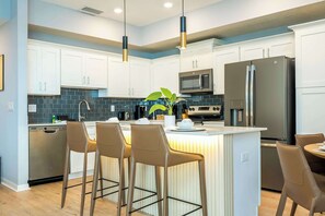 Una cocina moderna con armarios blancos, electrodomésticos de acero inoxidable y una isla central con taburetes de bar.