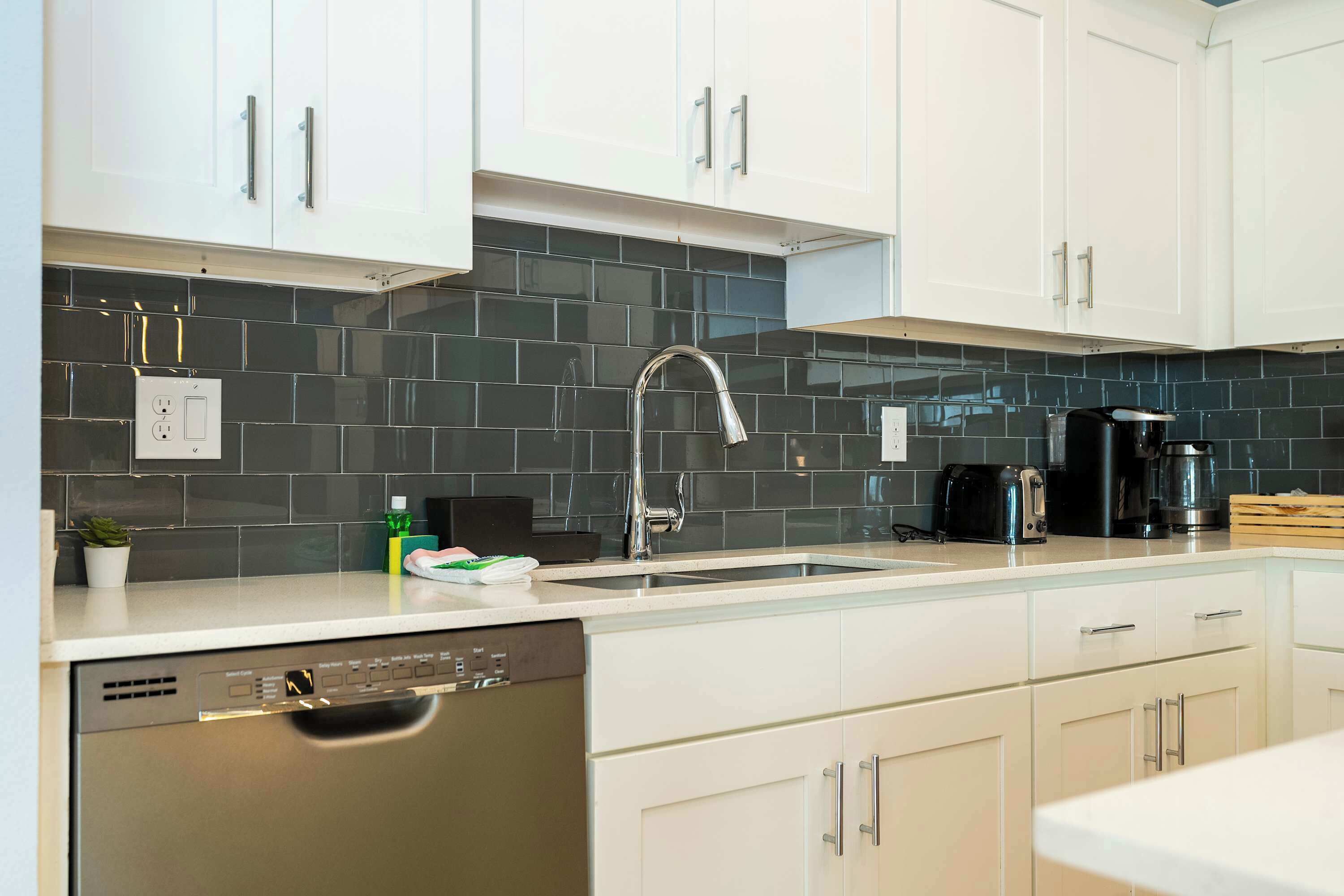A modern kitchen with white cabinets, a black tiled backsplash, a stainless steel faucet, and a dishwasher.