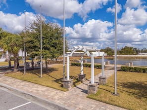 A park with a white pergola, stone pillars, and a paved walkway.