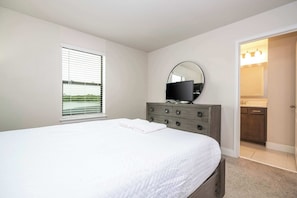 A bedroom with a bed, a dresser, a television, and a bathroom visible through an open door. - 6BR Villa Pool & Lake View Balmoral Resort (Haines City)