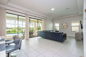 A spacious living area with a large window, a sofa, a dining table with chairs, and a pool view. - 6BR Villa Pool & Lake View Balmoral Resort (Haines City)