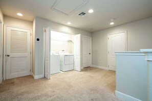 A hallway with white doors, a laundry area with a washing machine, and a thermostat on the wall.