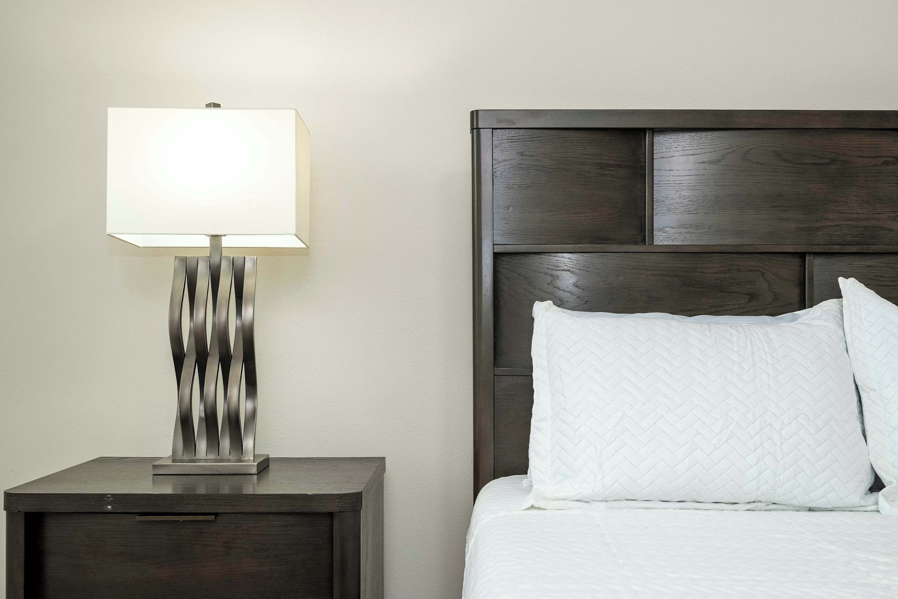 A bed with a quilted white pillow and a bedside table with a lamp.