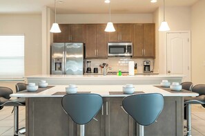 A modern kitchen with stainless steel appliances, a central island with bar stools, and pendant lighting. - 6BR Villa Pool & Lake View Balmoral Resort (Haines City)