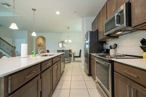 A modern kitchen with stainless steel appliances, a dining area with a chandelier, and a staircase leading to another level. - 6BR Villa Pool & Lake View Balmoral Resort (Haines City)