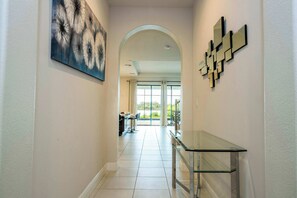 A hallway with a glass console table, a painting, and a geometric wall decoration. - 6BR Villa Pool & Lake View Balmoral Resort (Haines City)