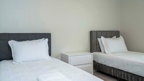 Hotellihuone, jossa on kaksi erillistä sänkyä, yöpöytä ja valkoinen lipasto.
