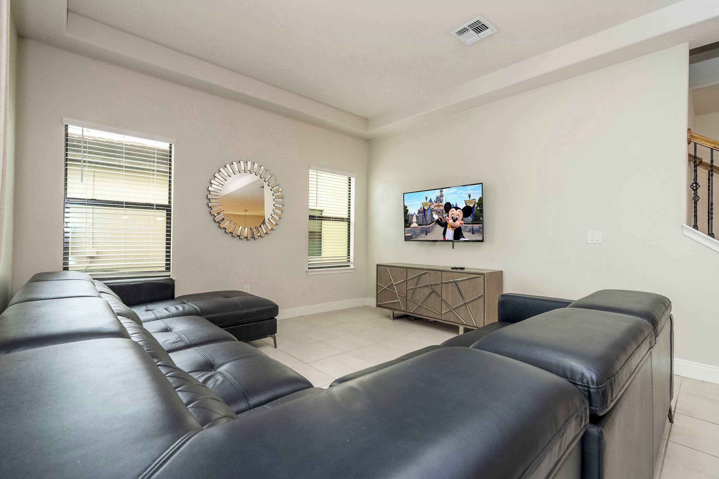 Una sala de estar con un sofá seccional, un televisor montado en la pared y un espejo decorativo.