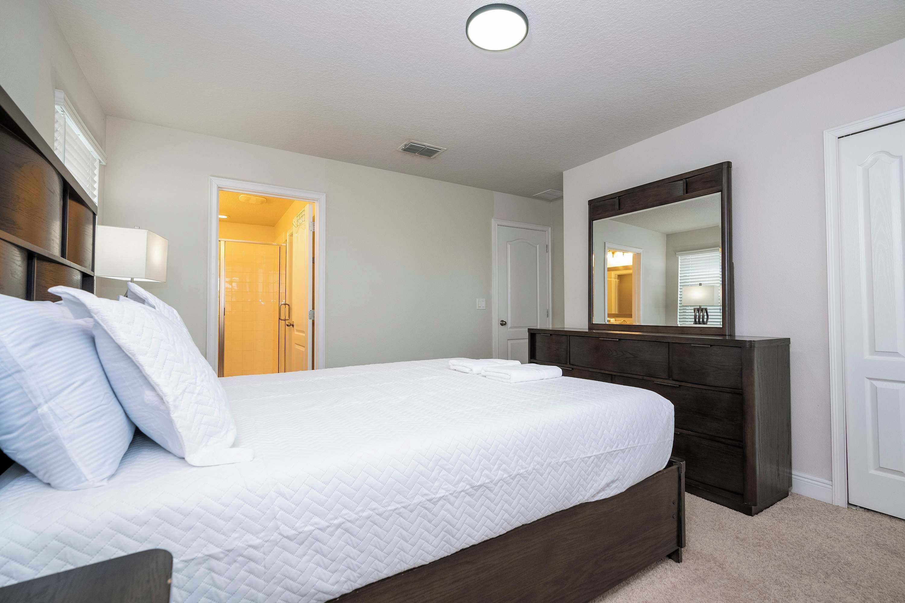 A hotel room with a large bed, a dresser, a mirror, and a door leading to a bathroom.