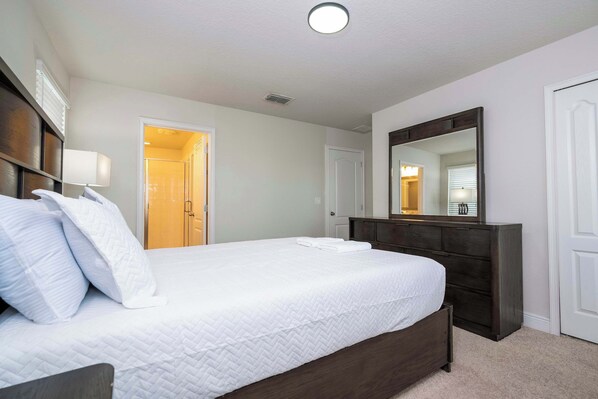 A hotel room with a large bed, a dresser, a mirror, and a door leading to a bathroom.