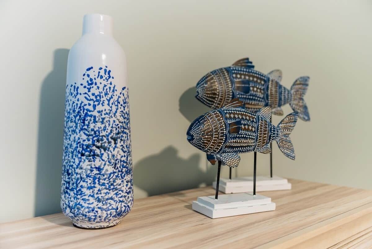 Un vase blanc orné de motifs bleus et une sculpture de poisson décorative posée sur une surface en bois.