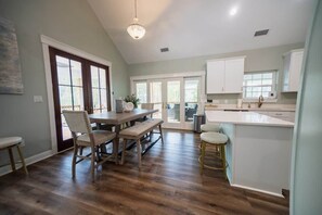 A kitchen with a dining area, wooden flooring, and a view through the glass door. - Island Oasis with Included Golf Cart (Dauphin Island)
