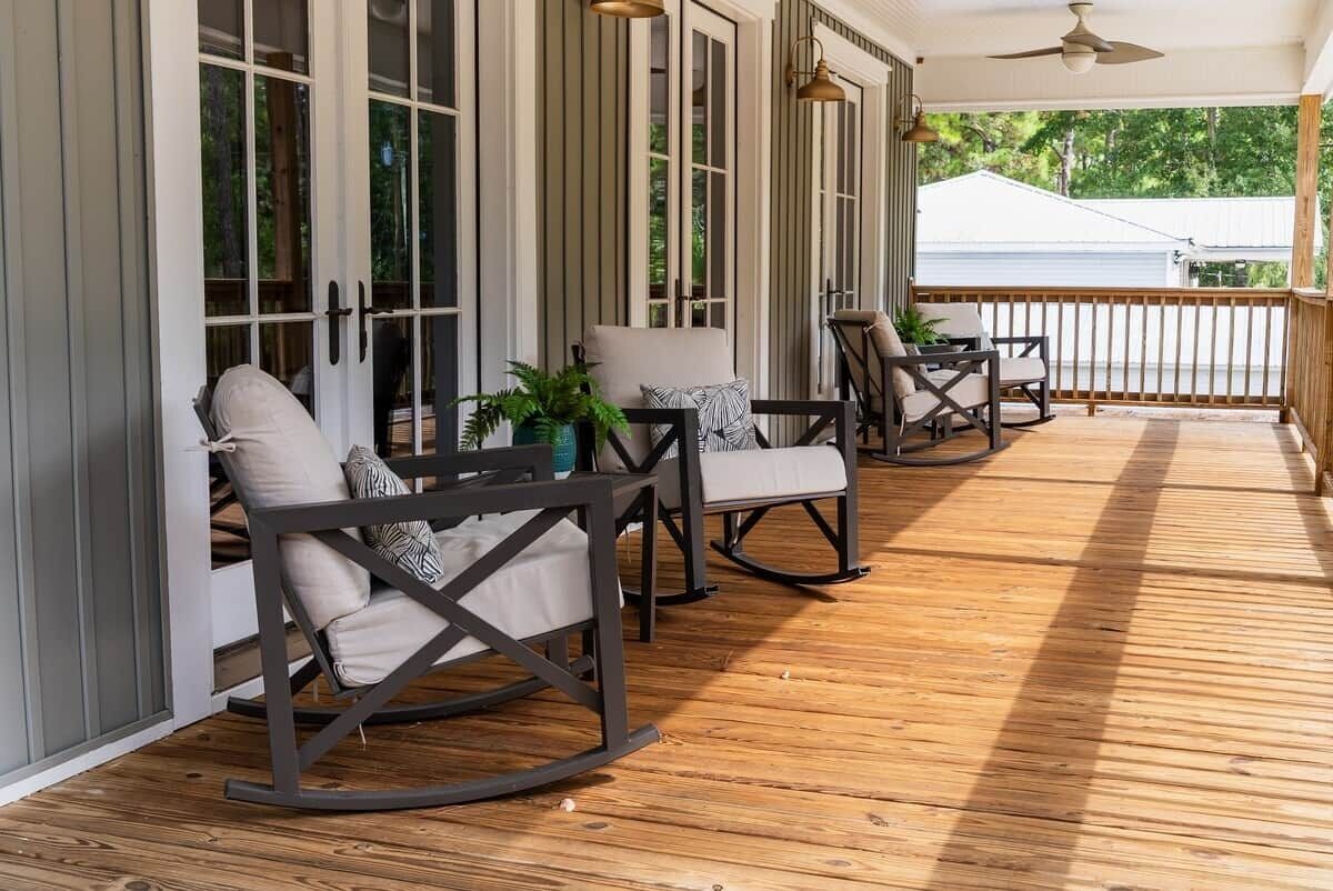 A covered porch with rocking chairs and a table, wooden flooring, and a ceiling fan.