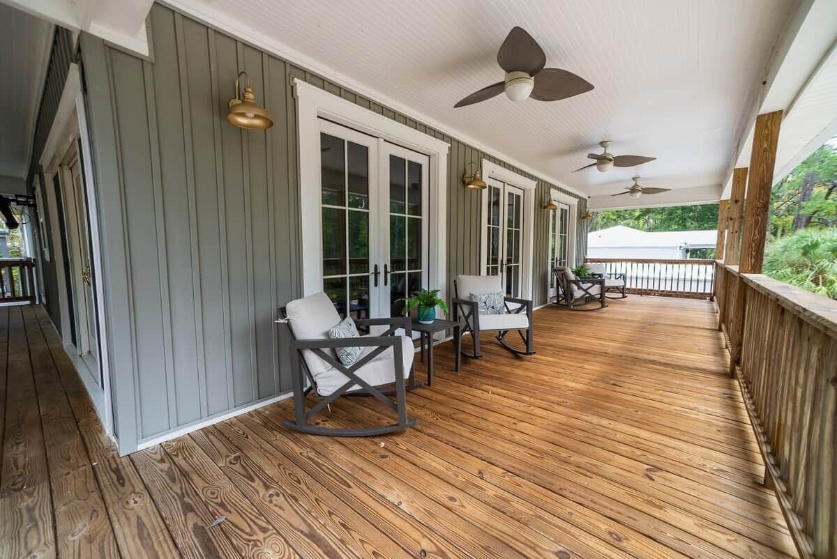 Een overdekt terras met houten vloer, een zithoek met stoelen en een tafel, en plafondventilatoren.