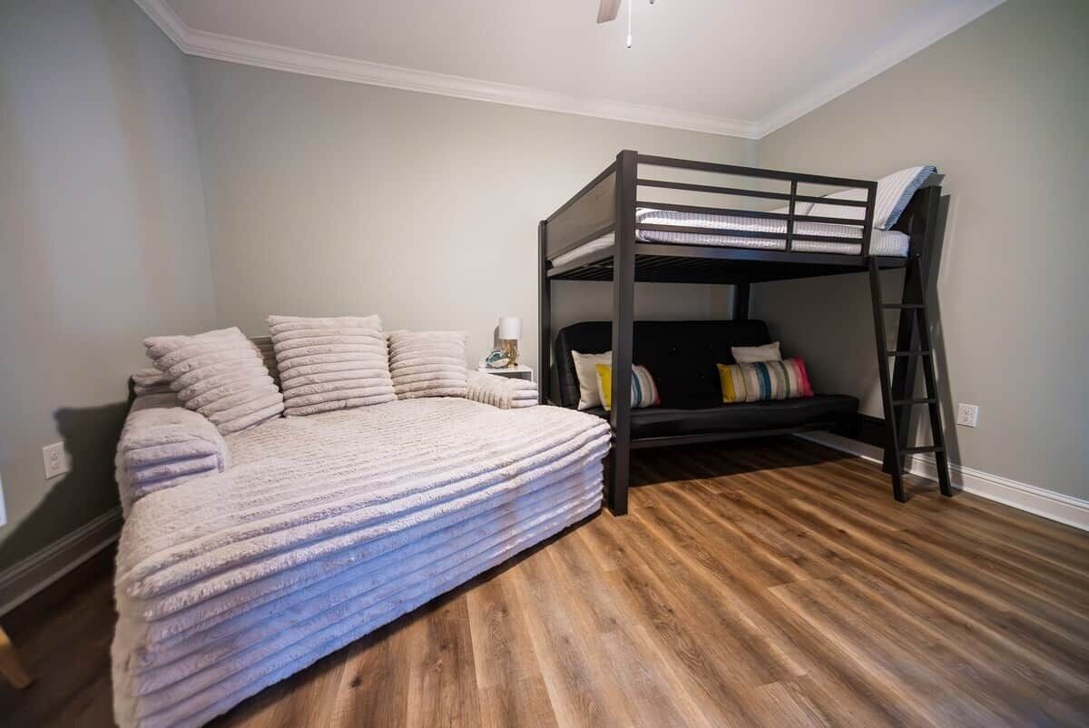 A room with a bunk bed, a daybed, and a wooden floor.