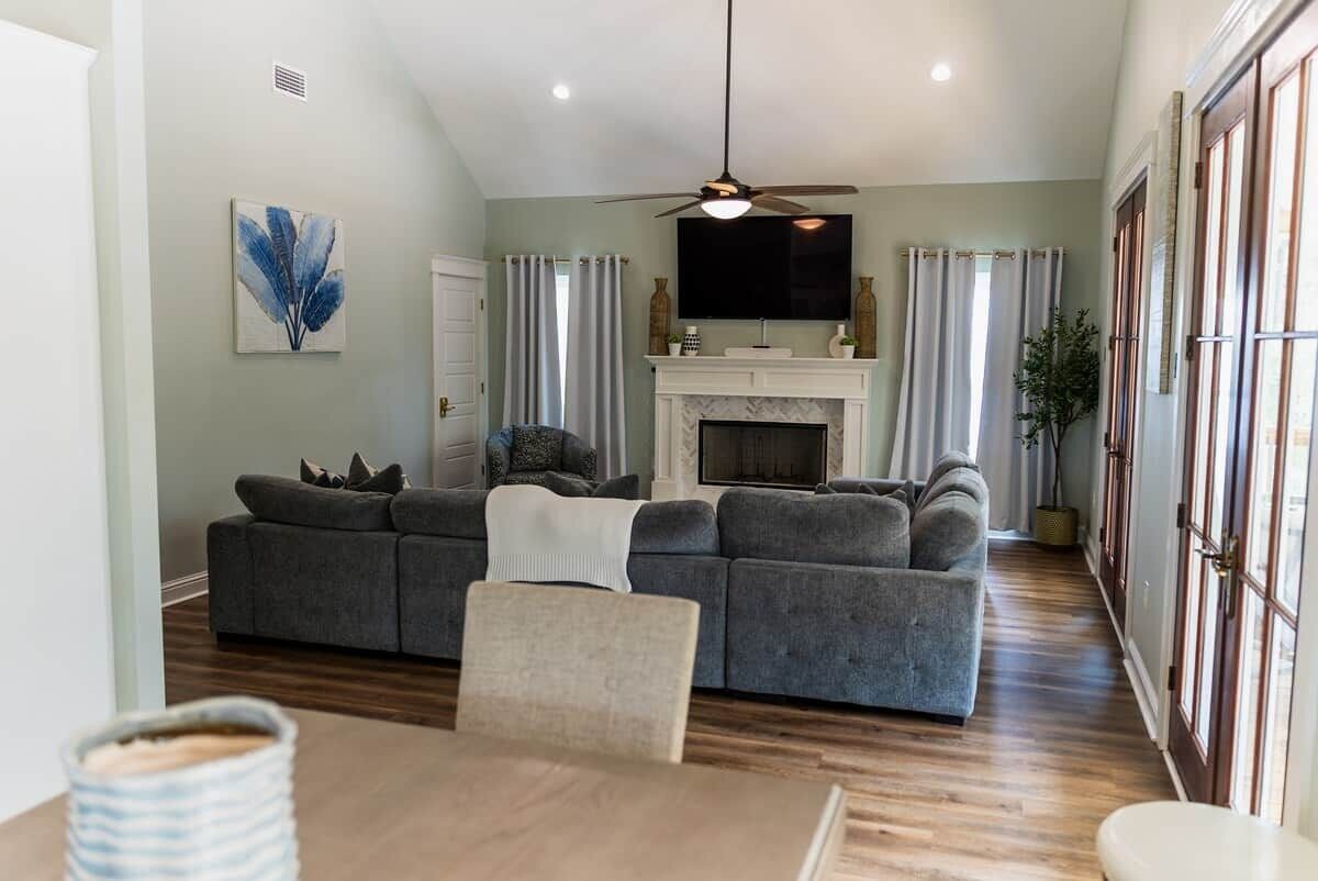 A living room with a grey sofa, a fireplace, a television, and a ceiling fan.