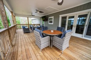 A covered outdoor patio with wicker furniture, a round table, ceiling fans, and a view of the surrounding area. - Island Oasis with Included Golf Cart (Dauphin Island)