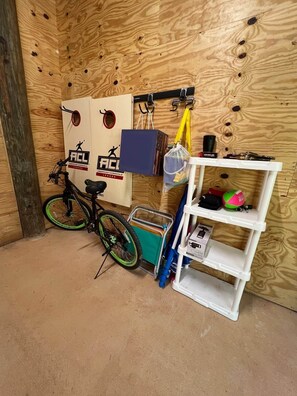A room with a wooden wall, a bicycle, a white shelf, and a blue storage box. - Island Oasis with Included Golf Cart (Dauphin Island)