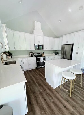 A modern kitchen with white cabinetry, a central island with stools, and a built-in oven. - Island Oasis with Included Golf Cart (Dauphin Island)