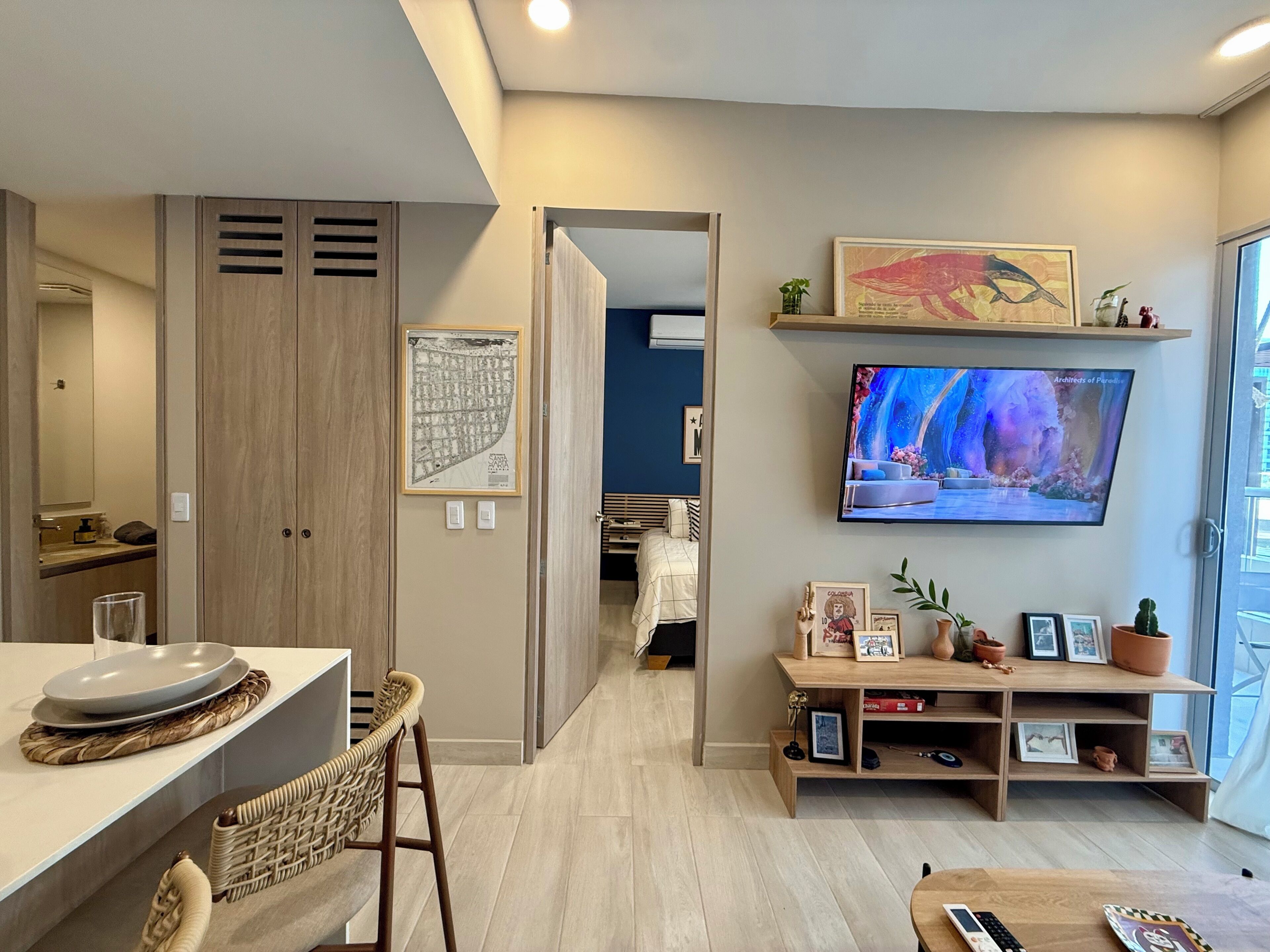 Ein modernes Wohnzimmer mit Fernseher, ein Essbereich mit Tisch und Stühlen sowie ein Flur, der zu einem Schlafzimmer führt.