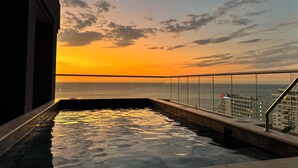 En pool på taget med udsigt til solnedgangen over havet, en glasgelænder og et Marriott hotel i baggrunden.