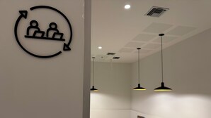 Et moderne interiør med et rundt skilt der viser to personer og en pil, en bænk og hængende lamper.