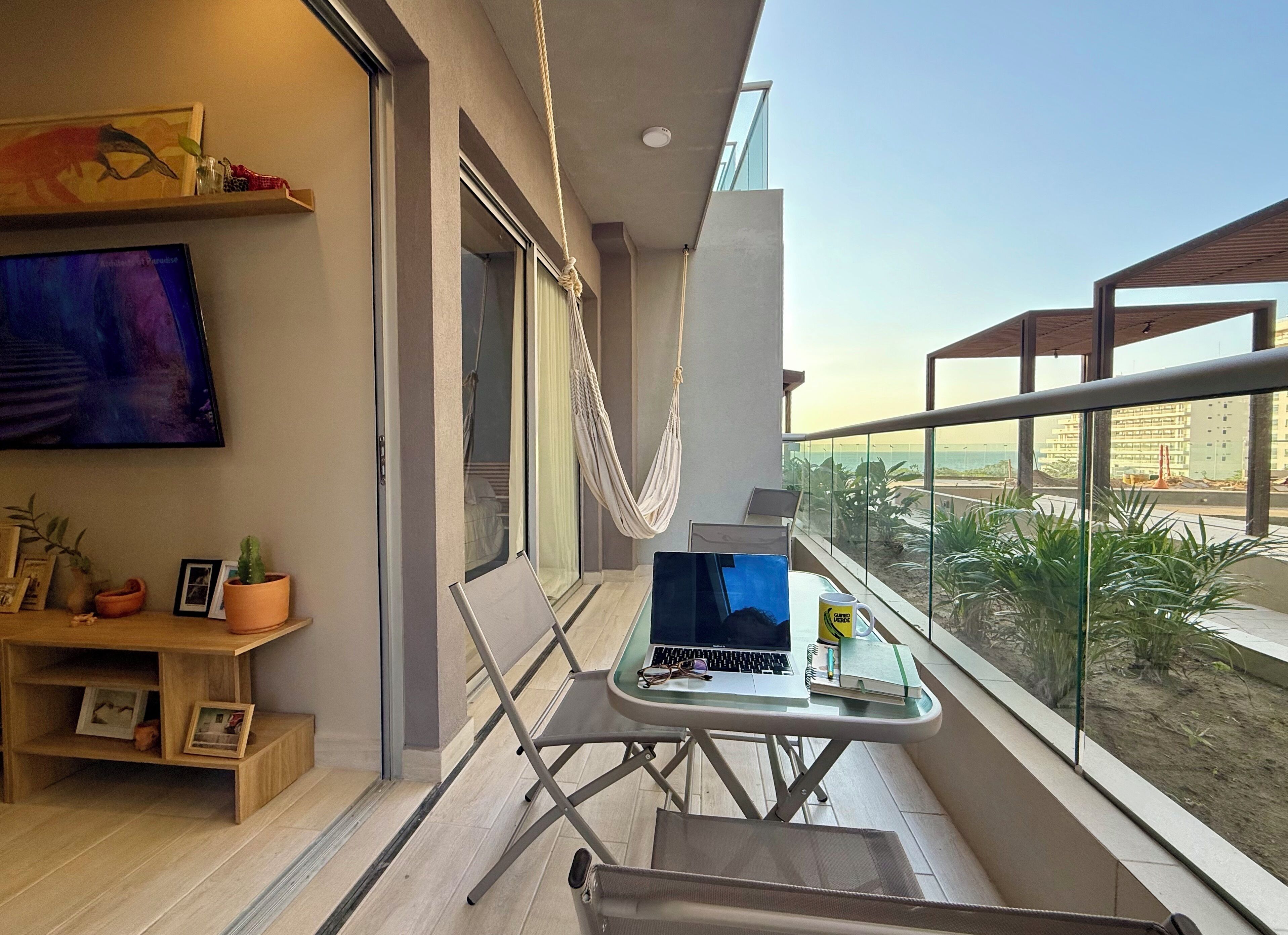 Ein Balkon mit einer Hängematte, einem Laptop und einer Kaffeetasse.