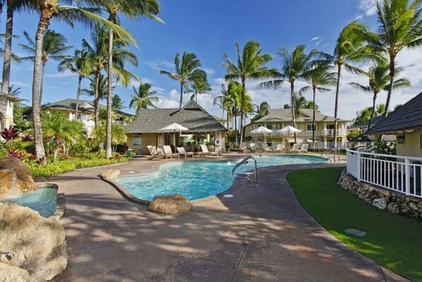 A resort pool area with lounge chairs, palm trees, and a clear sky.