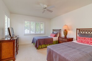 A bedroom with two beds, a ceiling fan, a bedside lamp, and a television on a dresser.