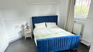 Ein Schlafzimmer mit einem Bett, einem Nachttisch, einer Lampe und einem Fenster.