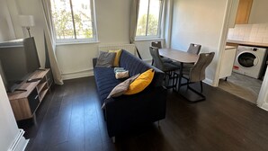 Ein kompakter Wohnraum mit Sofa, Esstisch, Fernseher und Waschmaschine.